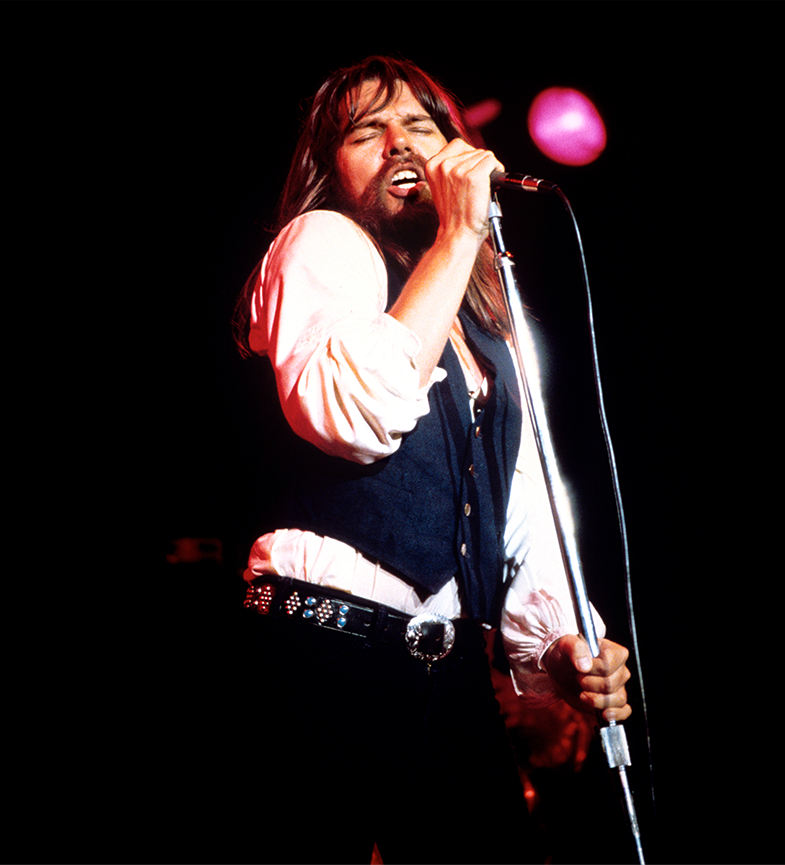 Young Bob Seger singing on stage with eyes closed.